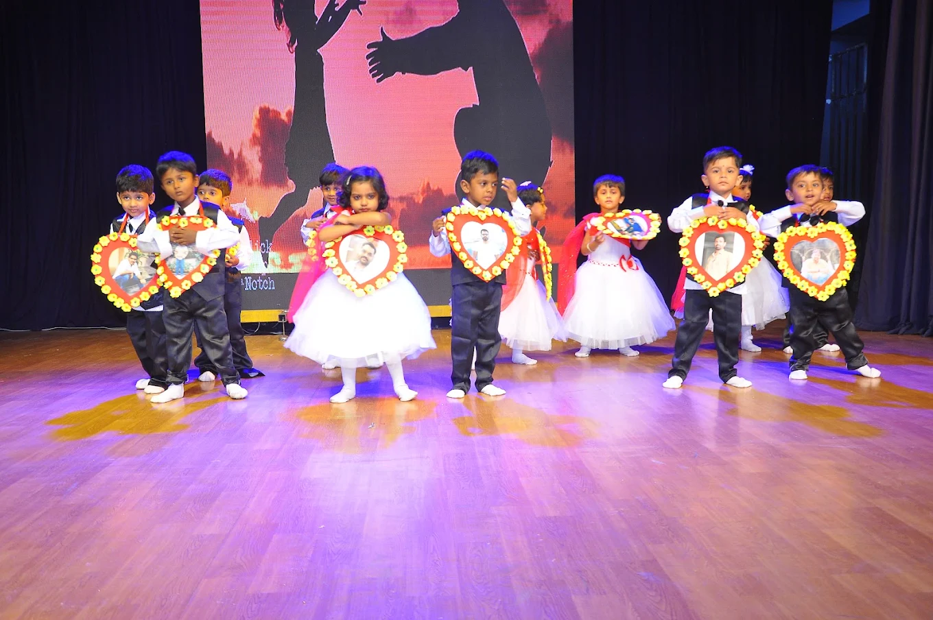 Children dancing with heart-shaped frames on stage at Star Kids Kingdom Annual Day